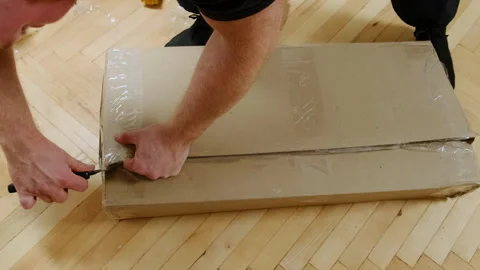 Man opens carton package with boards cutting adhesive scotch tape Video stock 304400176