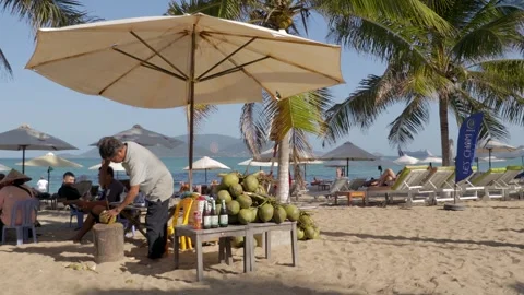 A man opens a coconut with a machete against the background of palm trees Video stock 262532996