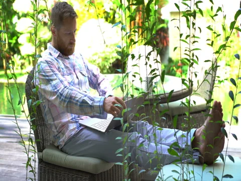 Man opens laptop and starts using it in exotic garden Stock Footage 79380130