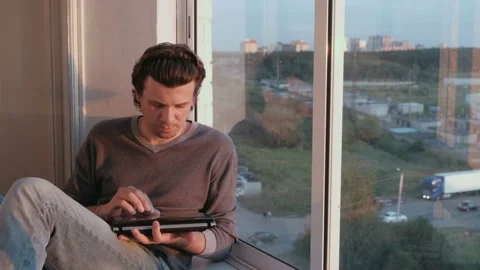 Man opens a netbook and starts to work sitting on the balcony at sunset. Video stock 102449457
