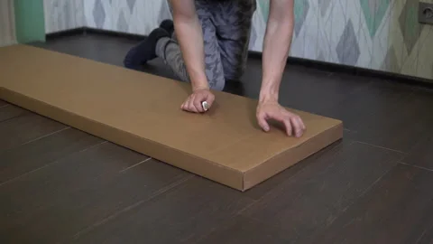 A man opens a new box with accessories for assembling a cabinet with a knife Stock Footage 131426054