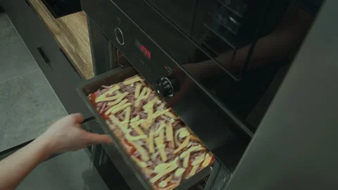A man opens the oven door and puts a large pizza on a tray to cook, cooking Stock Footage 155316487
