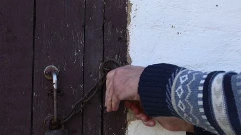 A man opens a padlock on a wooden door with a key. Stock Footage 289015341
