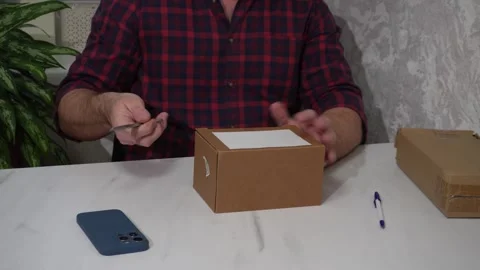 The man opens the parcel with the order and takes out a white mug from the 스톡 동영상 305024843