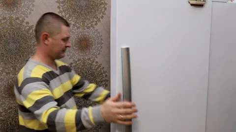 A man opens the refrigerator in the kitchen and takes a ripe tangerine from Stock Footage 167650463