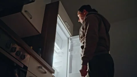 A man opens a refrigerator at night and takes an apple from it, viewed from Stock Footage 309558621