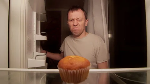 A man opens the refrigerator at night on the shelf is one cupcake, a disgruntled Stock Footage 144788584