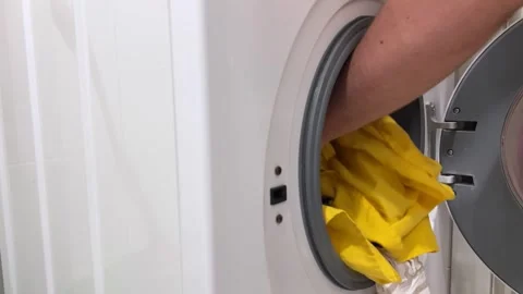 Man opens round glass door and puts dirty laundry into white washing machine Stock Footage 292033565