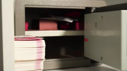 A man opens a safe and puts Chinese cash in it 스톡 동영상 277934414