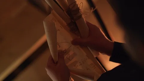 The man opens the scroll and looks at the written task / riddle. Room dim light. 스톡 동영상 108042710