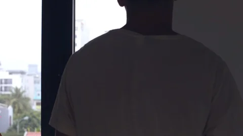 A man opens a window and stands looking at the city with multi storey buildings. Stock Footage 127672929