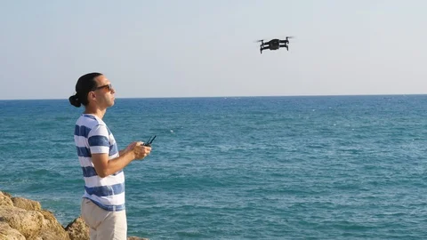 Man operate small flying quadcopter at sea shore, windy weather Stock Footage 105198674