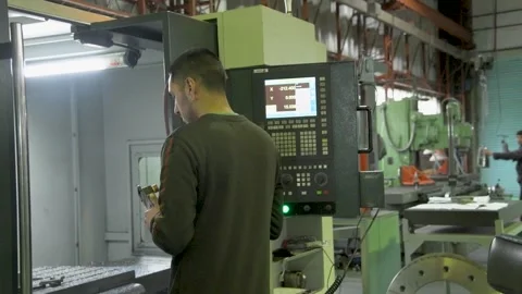 Man operates a CNC machine in an industrial workshop with bright lighting and Stock Footage 295091115