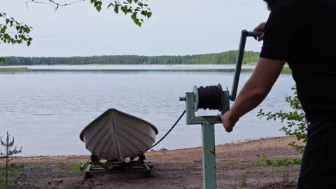 Man operates a hand winch to lower a boat into the lake. Horizontal slow-motion. Stock Footage 341361354