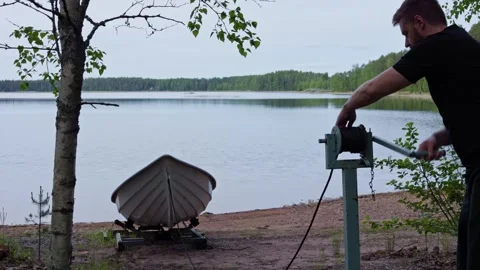 Man operates hand winch to pull a rowing boat onto a lake shore. Horizontal. Stock Footage 341361357