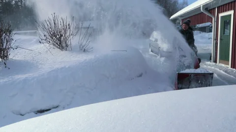 A man operates a snow blower to remove deep snow from his driveway in a res.. Stock Footage 287073442