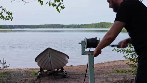 Man operates a winch to lower a rowing boat into the lake. Horizontal. Stock Footage 341361358