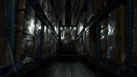 Man operating and ascending forklift machinery in darkened aisle of warehouse. Stock-Footage 88028610