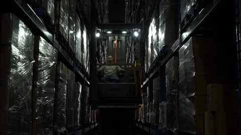 Man operating and elevating forklift machinery in darkened aisle of warehouse. Stock-Footage 88028726