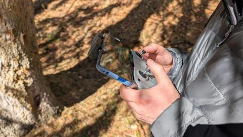 Man operating drone controller with smartphone outdoors in forest sunlight 스톡 사진