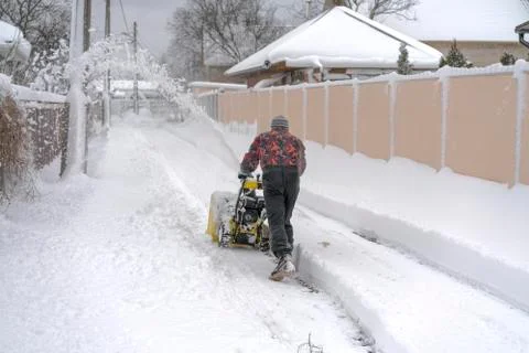 Man operating snow blower to remove snow on driveway Stock Photos