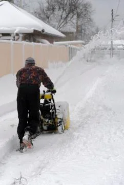 Man operating snow blower to remove snow on driveway. A man cleans the road f Stock Photos