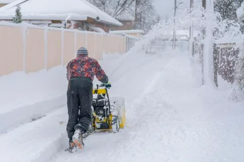 Man operating snow blower to remove snow on driveway. A man cleans the road f Stock Photos