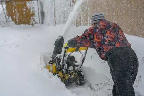 Man operating snow blower to remove snow on driveway. Man using a snowblower. Stock Photos