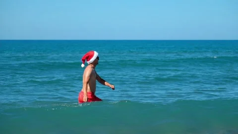 Man or guy in santa claus hat walking along sea on background of mountains. Video stock 253398172