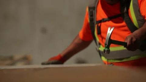 Man In Orange Construction Vest Uses Hammer to Pound Nail Stock Footage 106594084