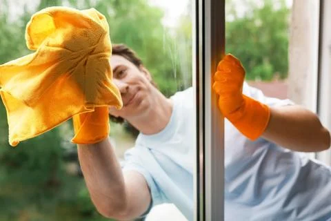 A man in orange gloves smiles while wiping a window with a yellow cloth. Th.. Stock Photos