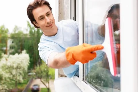 A man in orange gloves uses a squeegee to wash a window. This bright image .. Stock Photos