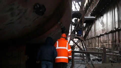 Man in an orange jacket and helmet, checks the work of welders at the dock Stock Footage 87614512