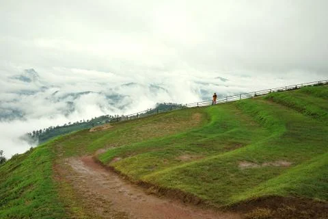 Man in orange jacket looking at view of mountain landscape with waves of fog Stock Photos
