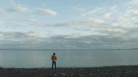 Man in orange jacket standing looking towards sea Video stock 88919918
