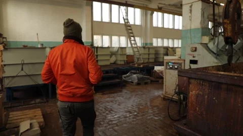 A man in an orange jacket walks through the old workshop of the factory Stock Footage 233071684