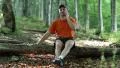 Man in orange t-shirt with red cell phone sits on a fallen tree in the forest HD Footage