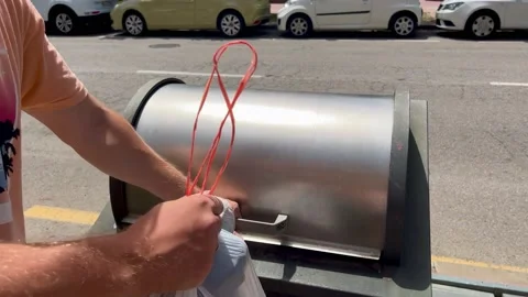 A man in an orange t-shirt throws a bag of garbage into a modern bin Stock Footage 201488116