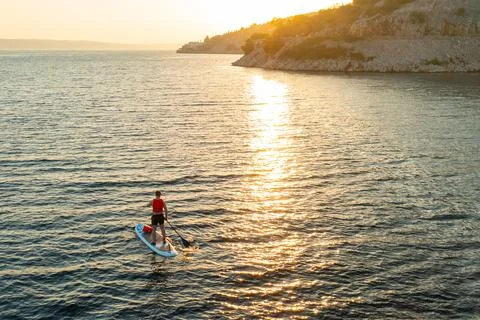 Man in an orange vest stands confidently on his paddleboard, moving across the Stock Photos