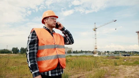 A man in an orange yellow and a construction helmet stands at a construction Stock Footage 129056655