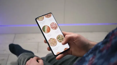 Man orders a pizza online, using a food delivery app on a smartphone 库存影片 147564511