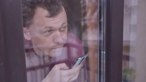 Man outside the window, looking at the street and using a mobile phone Stock Footage 155393990
