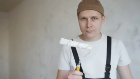 A man in overalls approaches the camera and paints the frame with a paint roller Stock Footage 144657129