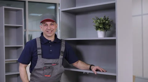 The man in overalls puts a pot of flowers on a cabinet shelf Stock Footage 61237390