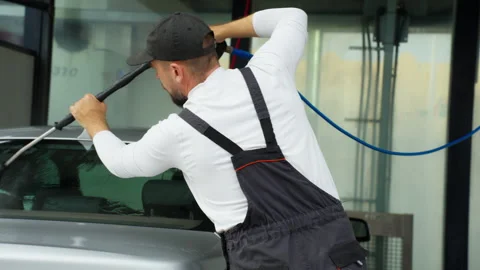 Man in overalls using a high-pressure spray gun to rinse and detail the rea.. Stock Footage 320890232