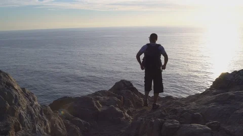 Man overlooking ocean from a cliff raising arms up in triumph, 4k Stock Footage 103437909
