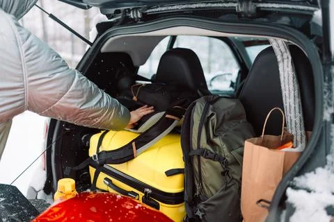 Man packing black backpack into full car trunk in winter Stock Photos
