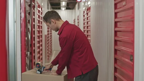 Man Packing Box with Adhesive Tape in Self Storage Warehouse Stock Footage 259826469