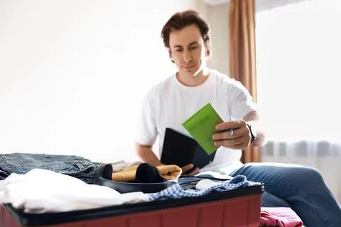 Man packing a red suitcase for summer vacation, holding his passport. Trave.. Stock Photos