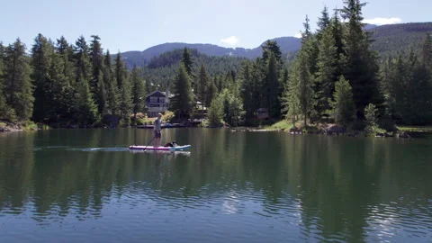Man paddle boarding on a pristine mountain lake on sunny day with his dog, stand Stock Footage 246611492
